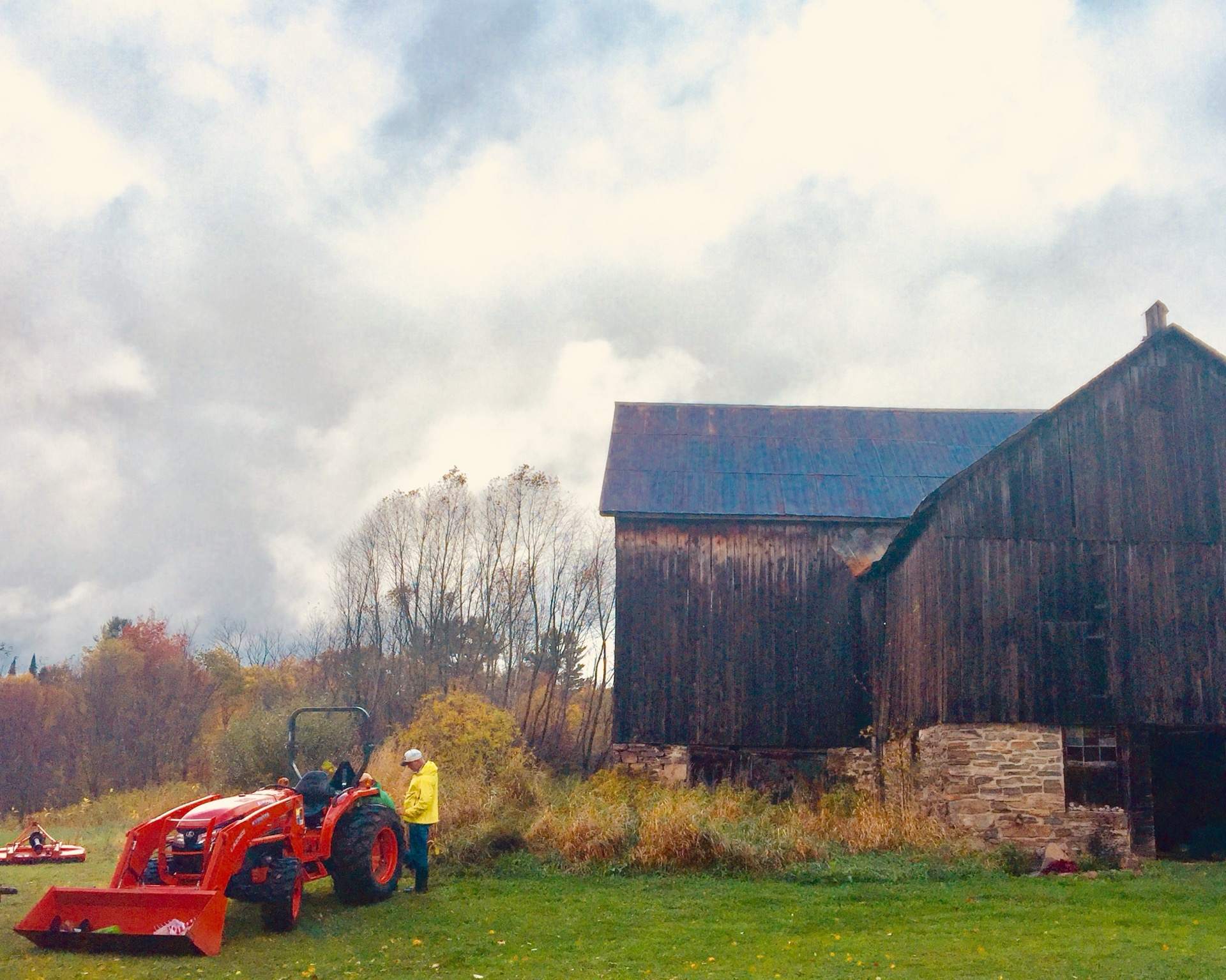 Barr Gilmore driving a red tractor past the weathered main barn at THE SON on an autumn afternoon